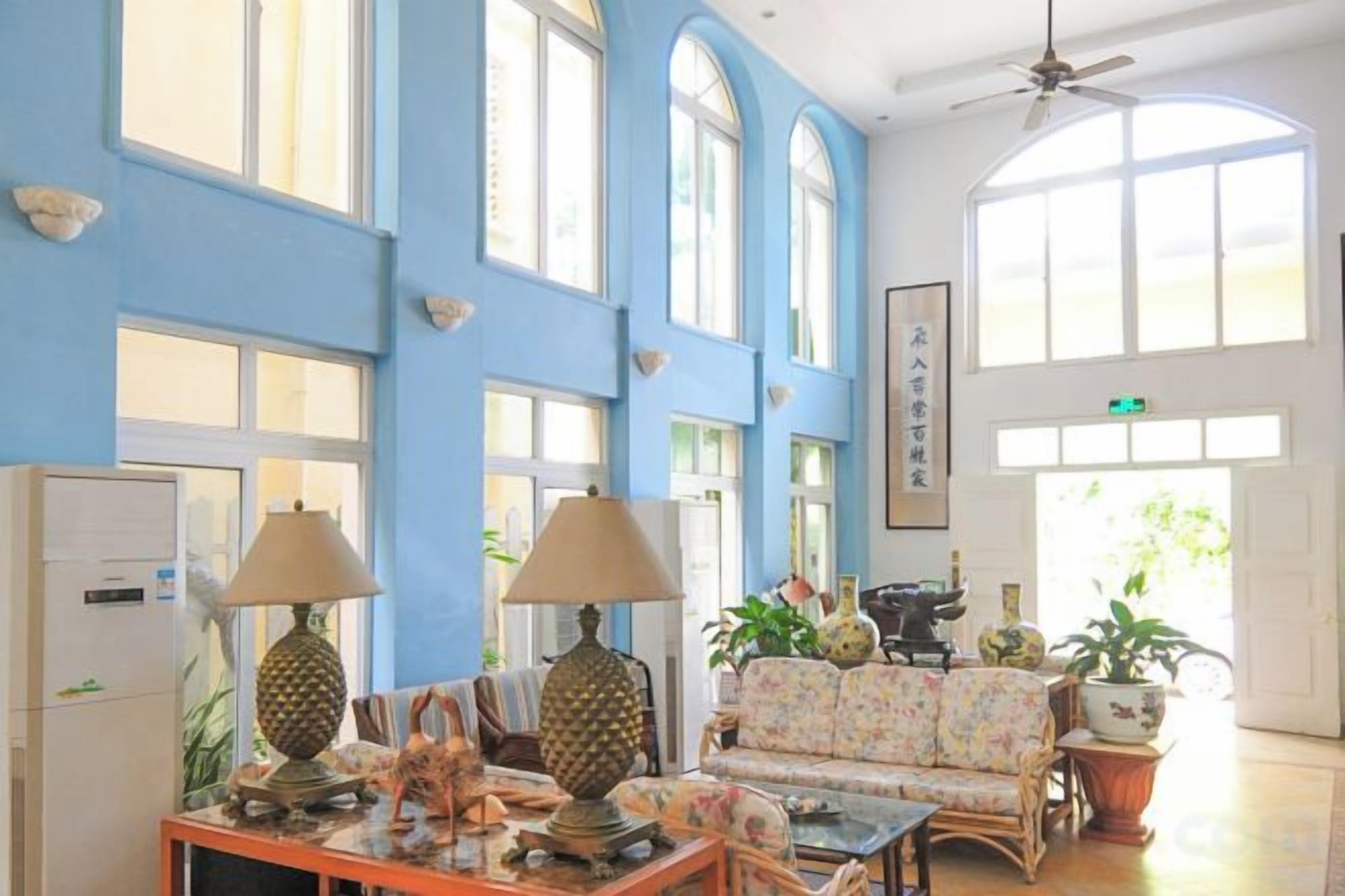 A spacious room with high ceilings, large windows, a ceiling fan, and a seating area with a sofa and table.