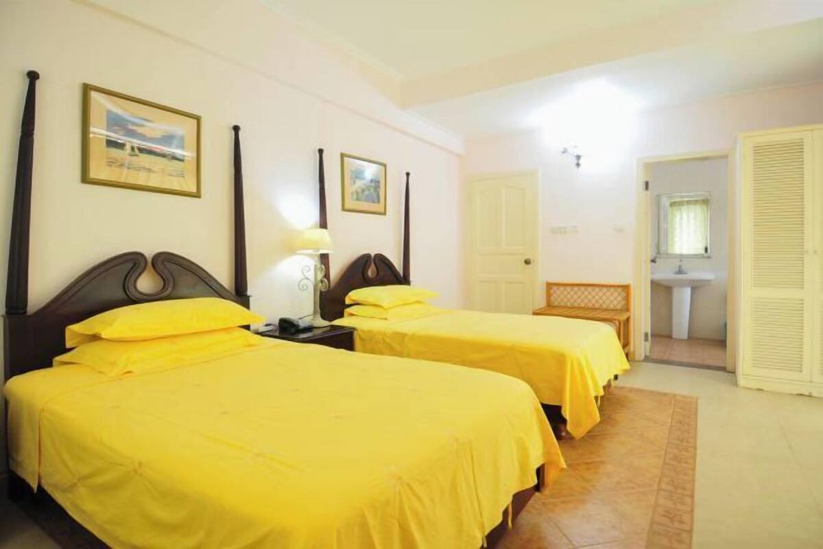 Une chambre d’hôtel avec deux lits, une table de chevet, une lampe, une porte et une salle de bain visible à travers une porte ouverte.
