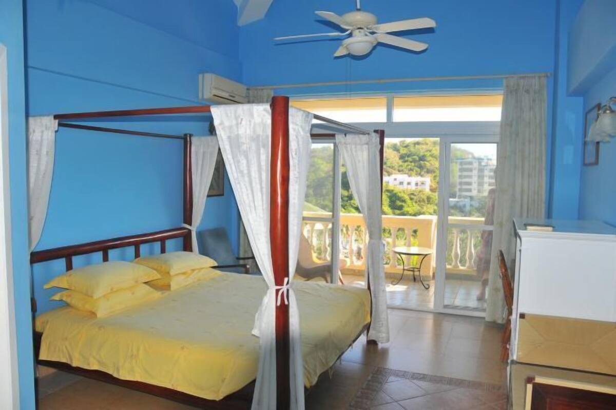 Un lit à baldaquin avec un ventilateur de plafond et un balcon agrémenté d’une table et de chaises.