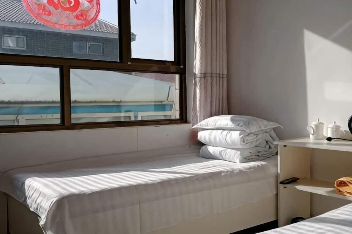 A room with a bed, a window, a desk, and a view of a building and water.