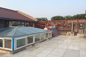 Un espace extérieur abrité, doté d’une structure en verre, d’un chauffe-eau solaire rouge et d’un bâtiment traditionnel avec un toit en tuiles.