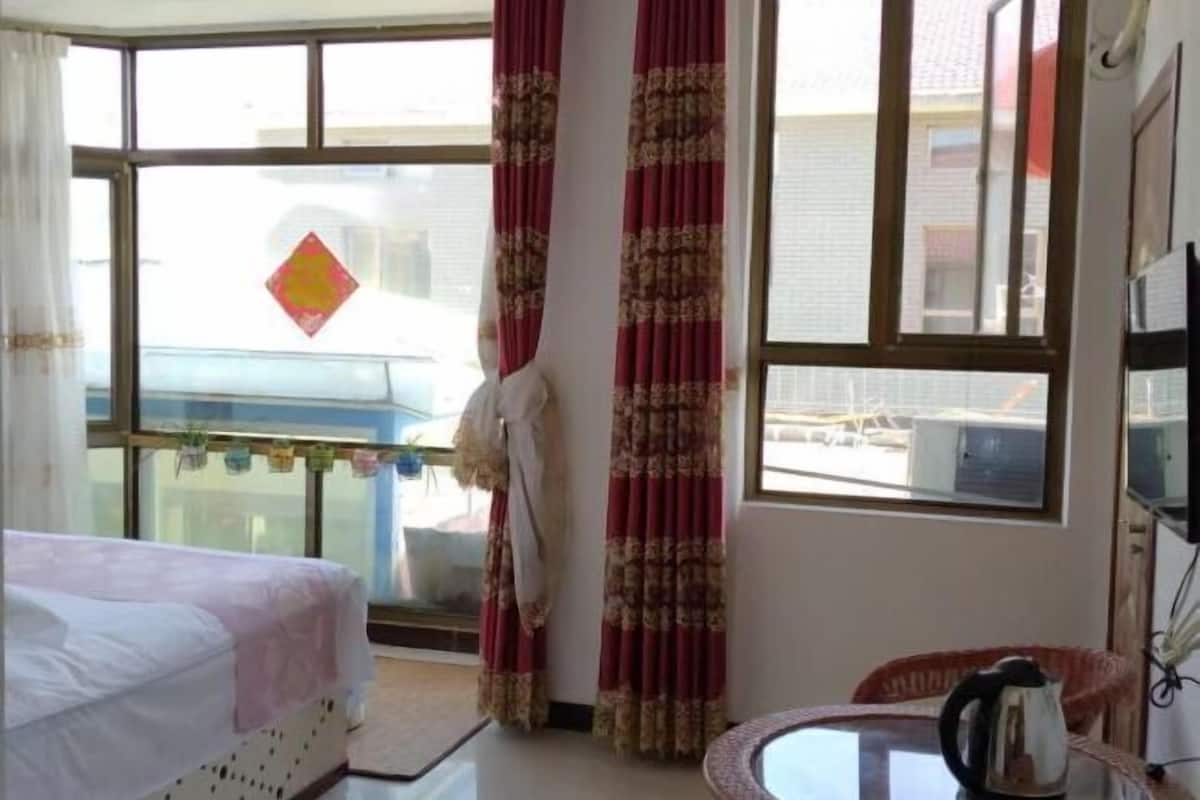 A hotel room with a bed, a table with a kettle, curtains, and a view of the outside.