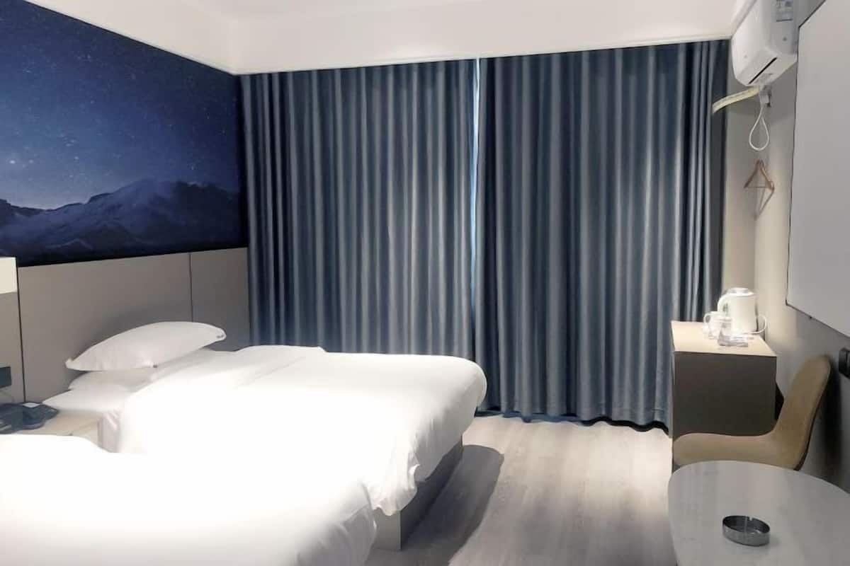 A hotel room with a bed, a night sky mural, a curtain, a bedside table with a coffee maker, and a small table.