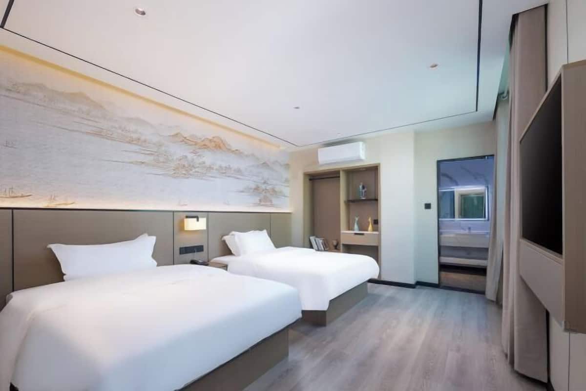 A hotel room with two beds, a large wall mural, a TV, and a built-in shelf.