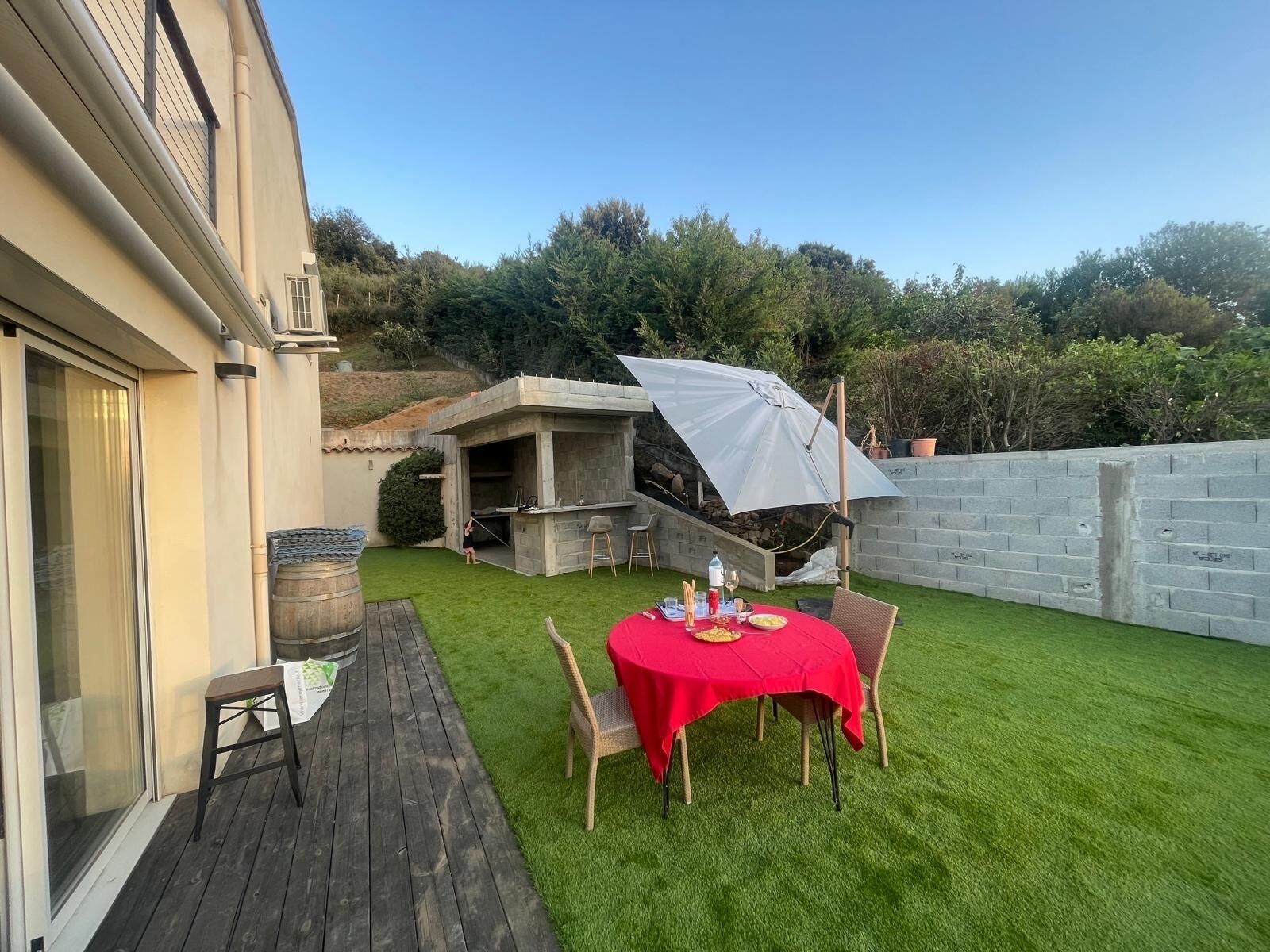 A patio with a red table and chairs, a barbecue area, and a wooden deck.