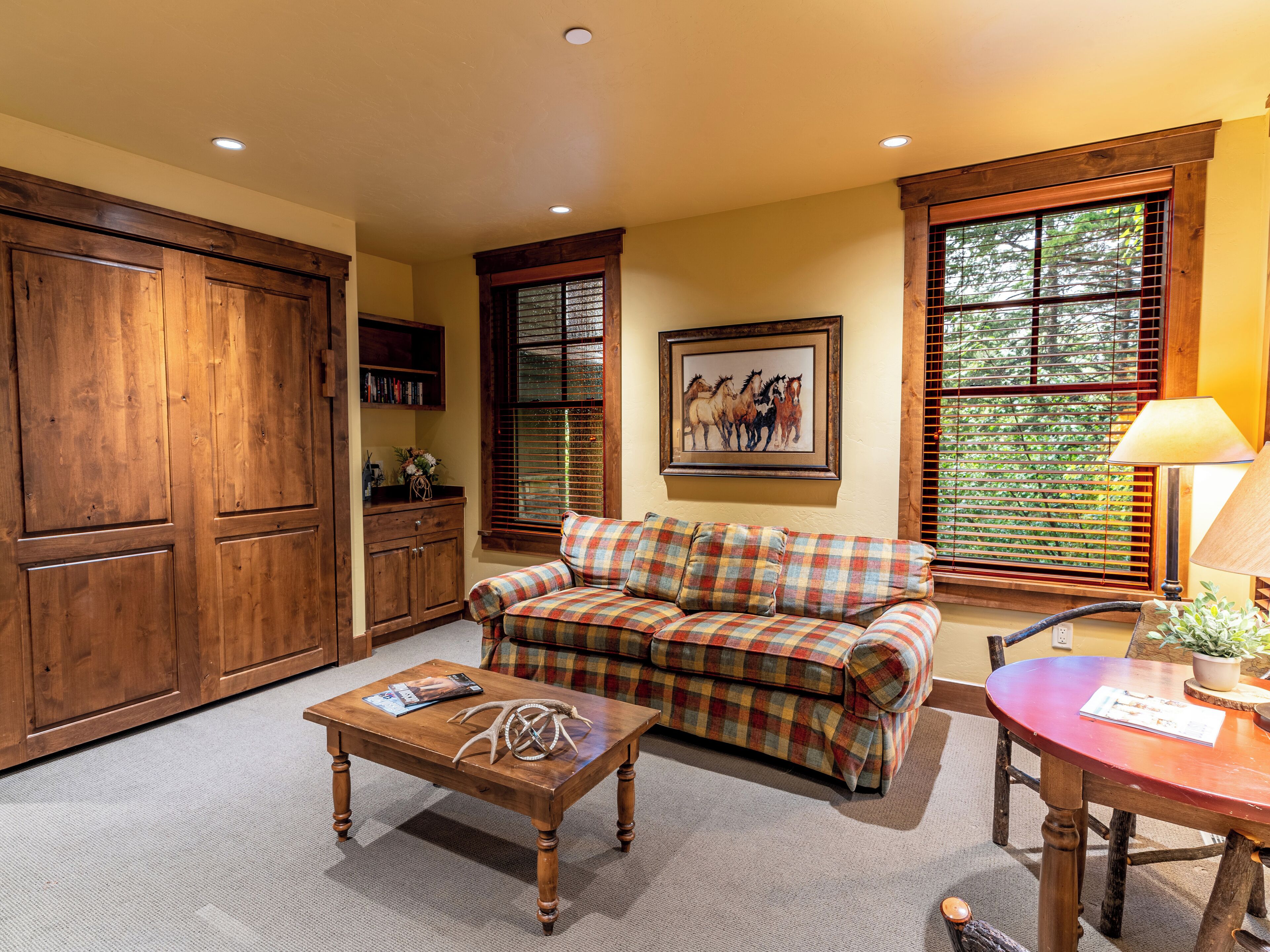 A cozy living room with a plaid sofa, a wooden coffee table, and a dining table with a lamp.