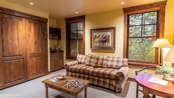 A cozy living room with a plaid sofa, a wooden coffee table, and a dining table with a lamp.