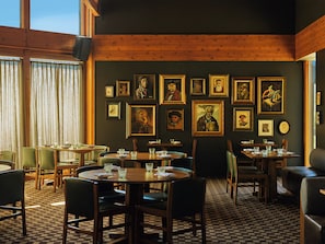 Um restaurante com paredes de madeira, diversas molduras com retratos e mesas com cadeiras.