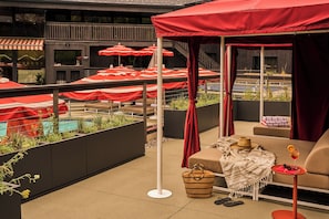 A rooftop terrace with outdoor seating, a pool, and red umbrellas.