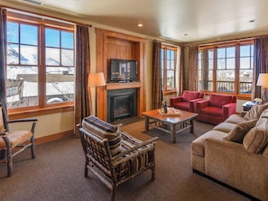A cozy living room with a fireplace, comfortable seating, and large windows offering a view of the outdoors. - Residences at Snow King (Jackson)