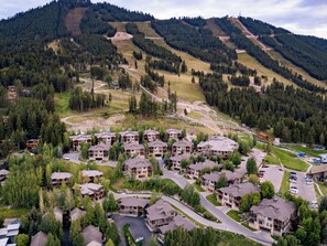 A residential area with multiple two-story houses, roads, and a hilly landscape with dense forests.