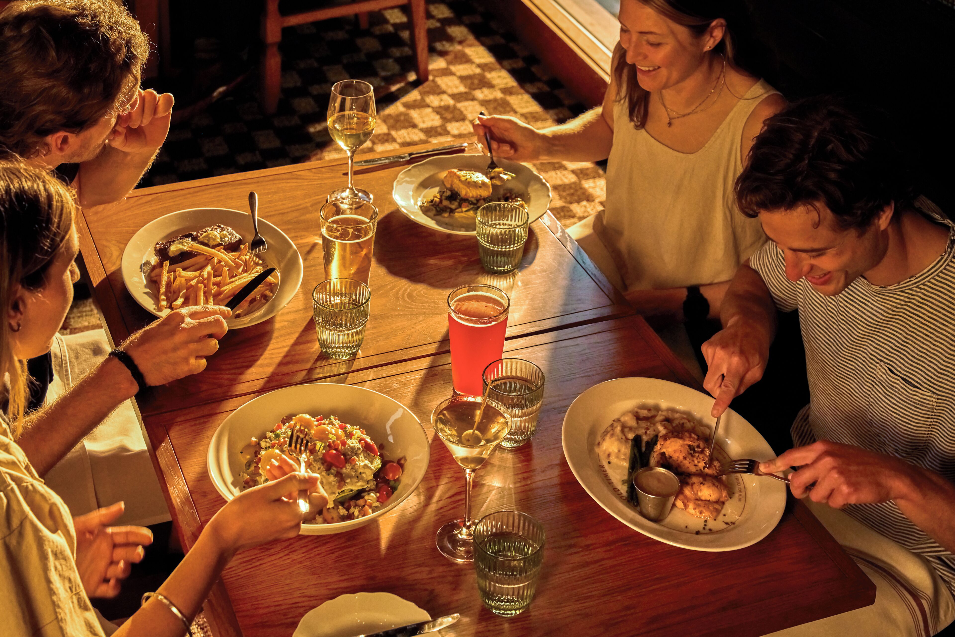 Un grupo de personas cenando en una mesa de madera con varios platos, vasos y cubiertos.