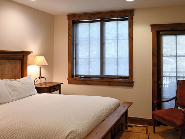Un dormitorio con una cama, una mesita de noche con lámpara, una ventana y una silla.