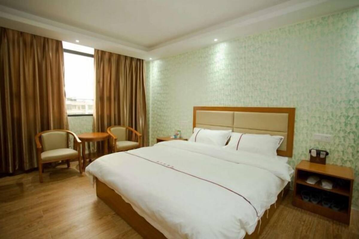 A hotel room with a large bed, two chairs, a small table, and a shoe rack.