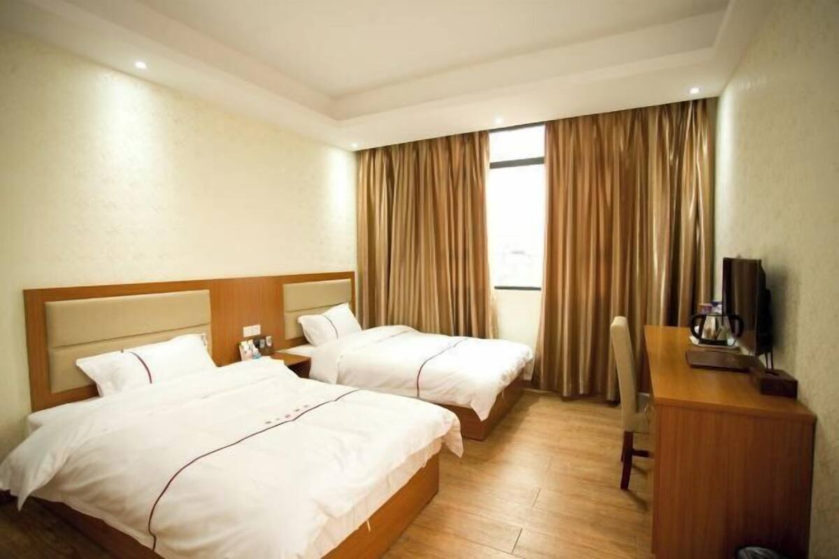 A hotel room with two beds, a desk, a chair, and a TV.