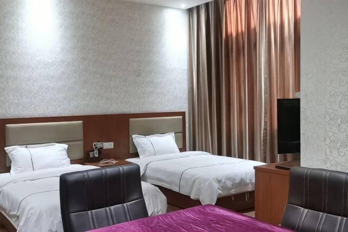 A hotel room with two beds, a desk, a chair, a television, and curtains.