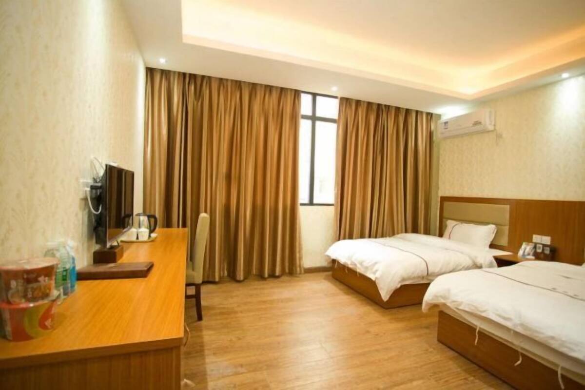A hotel room with two beds, a desk with a chair, a television, and an air conditioning unit.