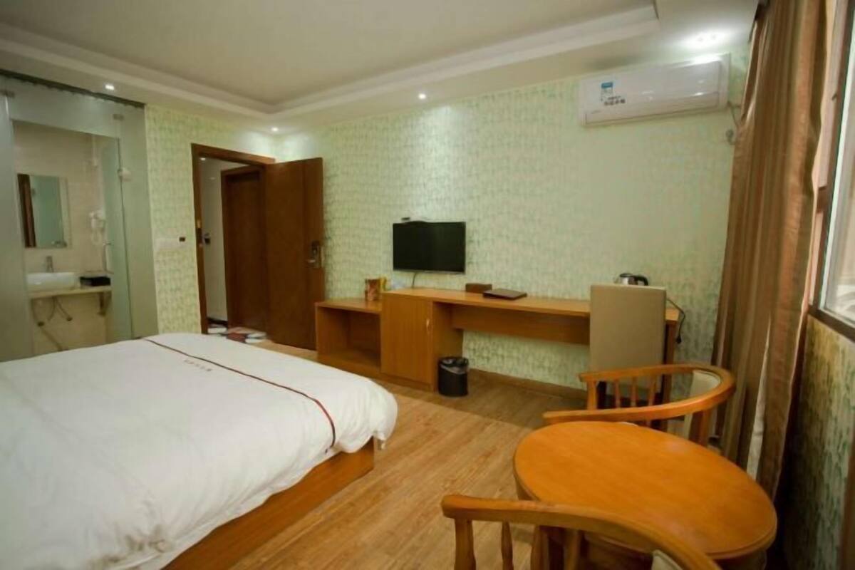 A hotel room with a bed, a desk, a chair, a television, and an air conditioning unit.