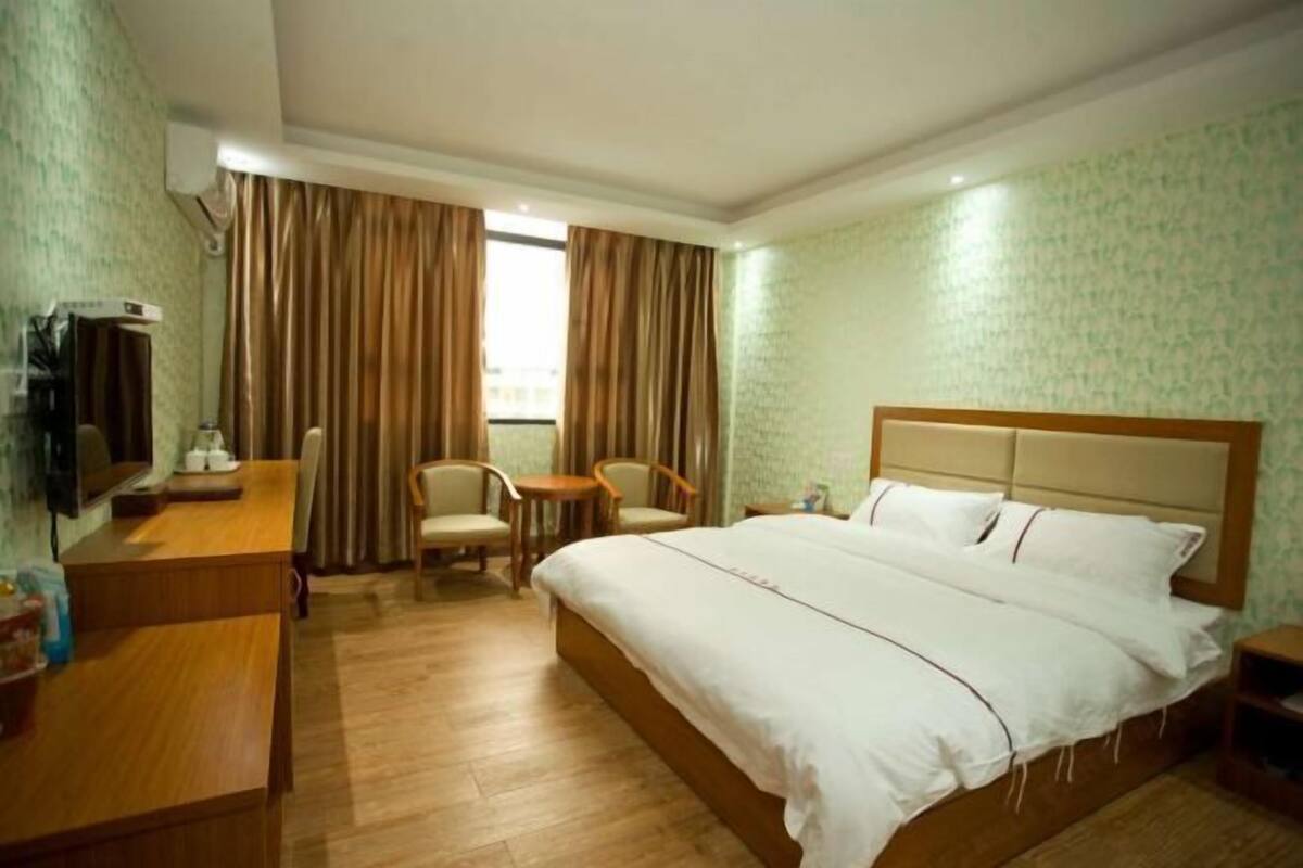 A hotel room with a bed, a desk with a chair, a TV, and curtains.
