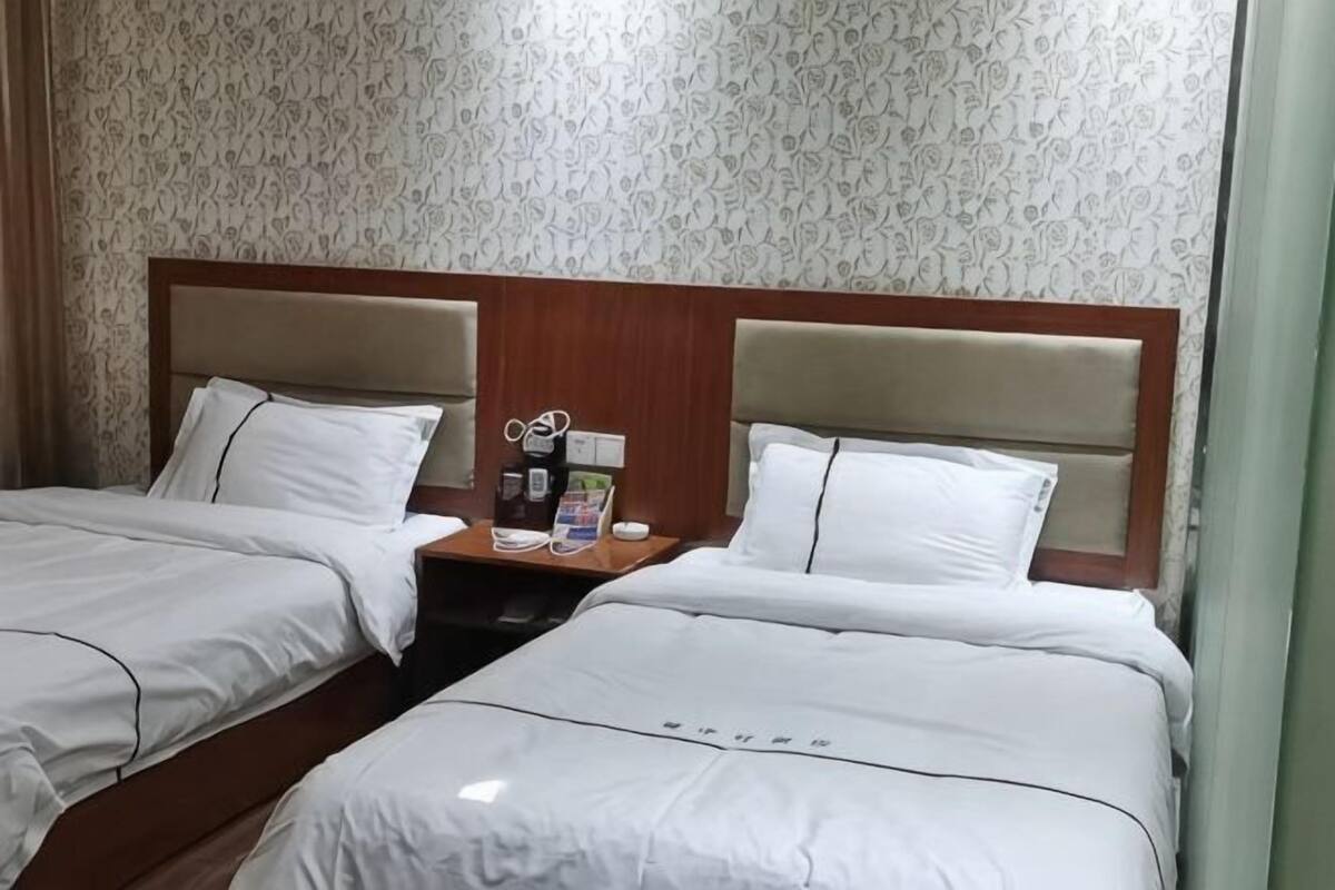 A hotel room with two beds, a wooden headboard, a nightstand with a coffee maker, and patterned wallpaper.