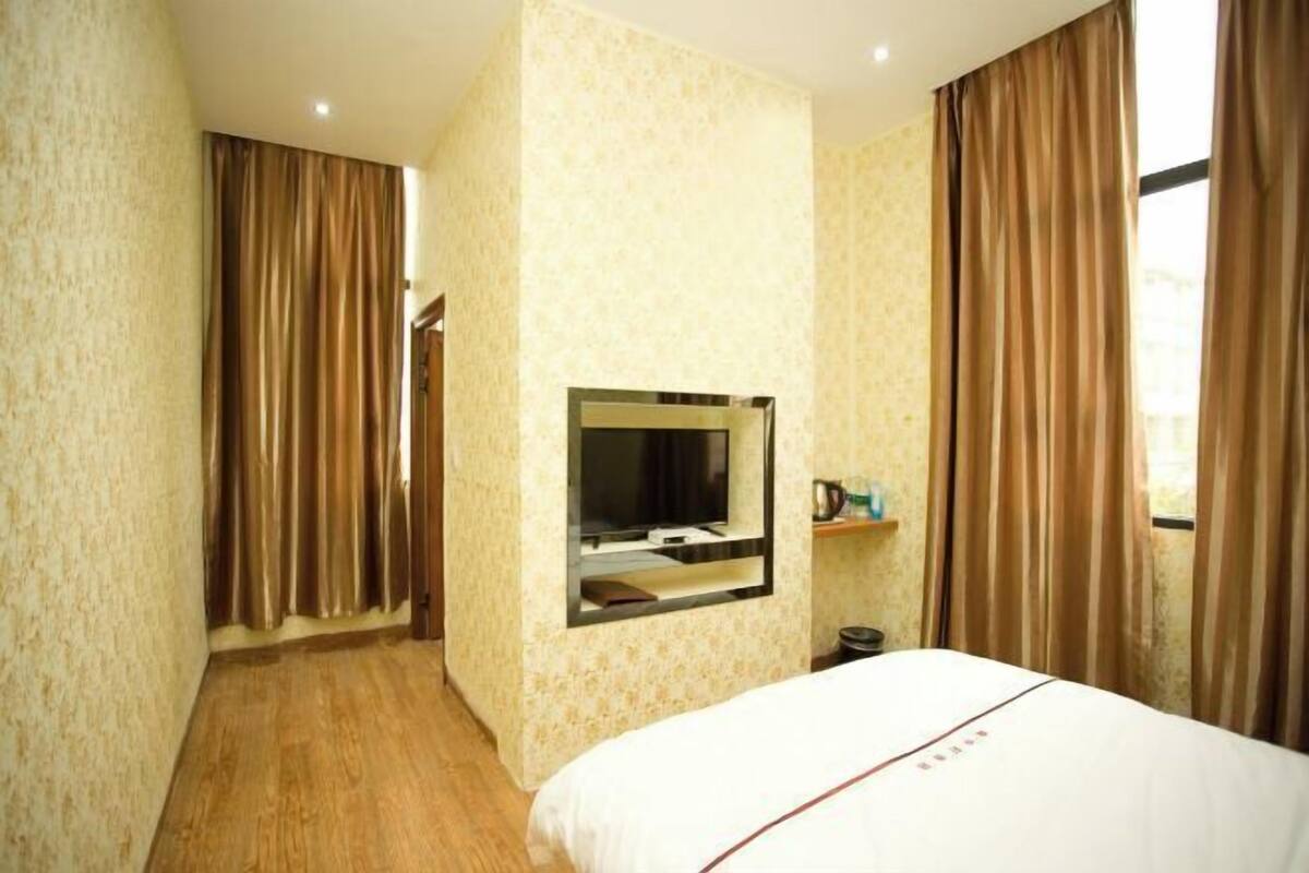 A hotel room with a bed, a television mounted on the wall, and curtains on the windows.