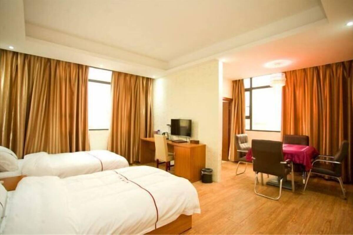 A hotel room with two beds, a desk with a television, a chair, and a table with a red tablecloth.
