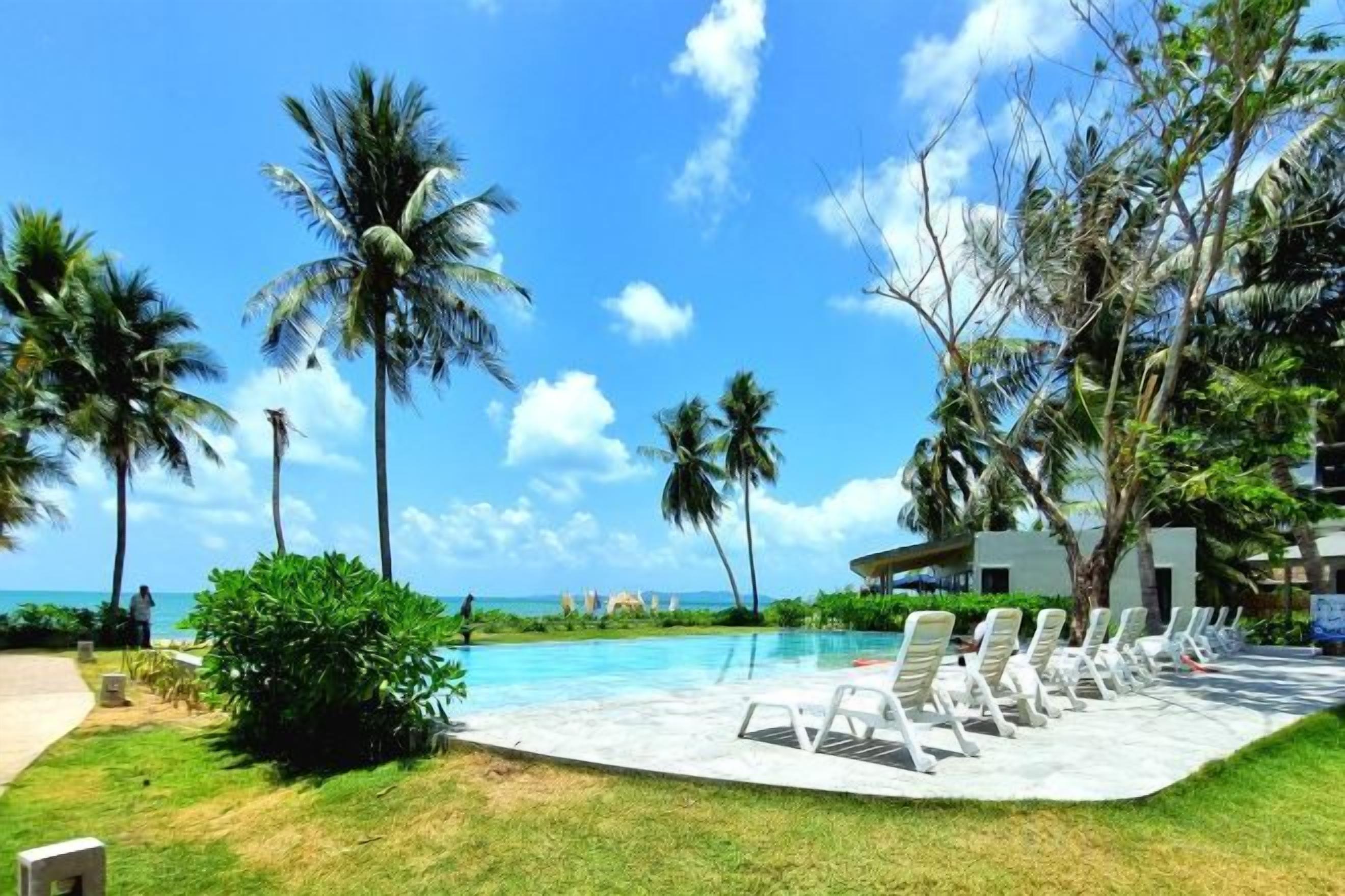 A poolside area with lounge chairs, palm trees, and a view of the ocean.