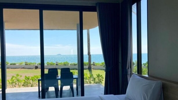 A hotel room with a large bed, a view of the sea, and a balcony with chairs. - Rayong Chalet Hotel and Resort (Klaeng)