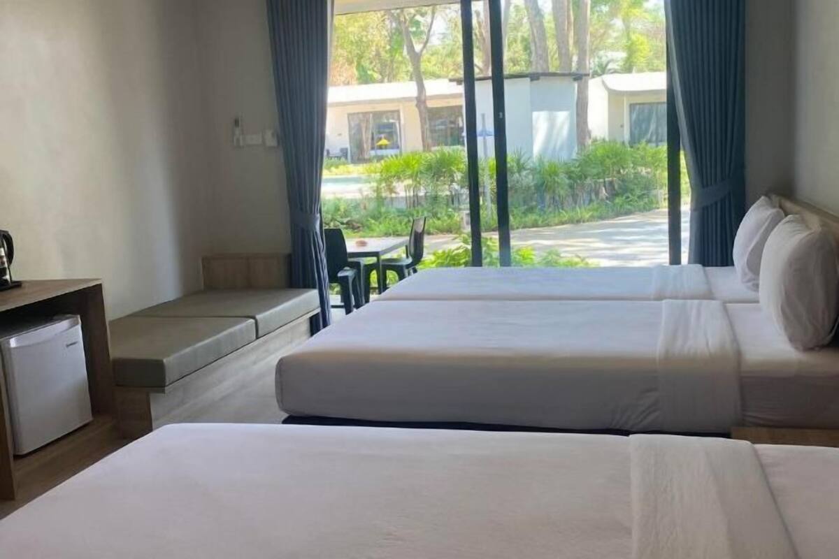 A hotel room with two beds, a small desk, and a view of the outdoors.