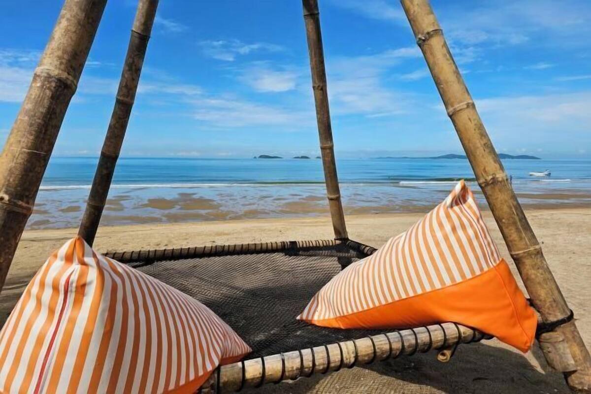 A beach hammock with striped pillows, a clear view of the ocean, and distant islands.