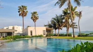 A swimming pool with a clear view of the ocean, surrounded by palm trees and a modern building. - Rayong Chalet Hotel and Resort (Klaeng)