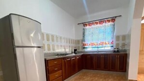 A compact kitchen with a refrigerator, wooden cabinets, and a patterned window.