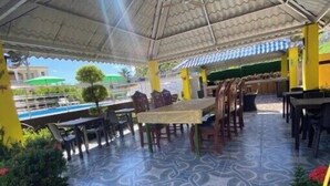 An outdoor patio area with a tiled floor, tables, and chairs under a covered structure.
