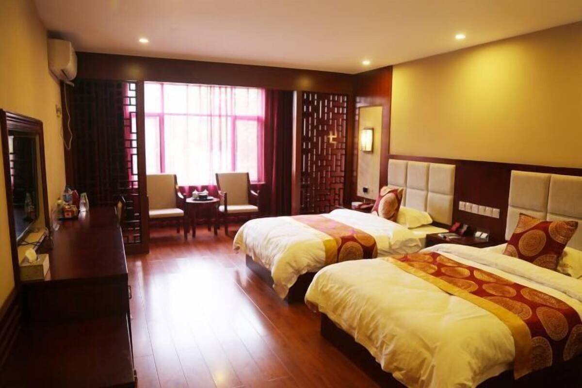 A hotel room with two beds, a desk, a chair, a TV, and a window with curtains.
