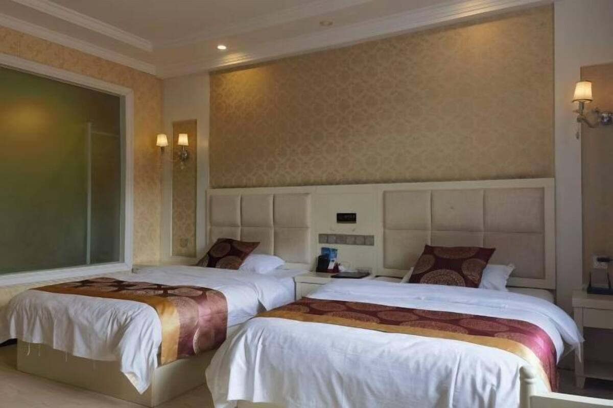 A hotel room with two beds, a large window, and a wall-mounted light fixture.