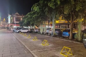 A nighttime street scene with parked cars, trees, and illuminated buildings.