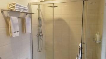 Cabina de ducha con paredes de vidrio, cabezal de ducha de mano y toallero con toallas dobladas.