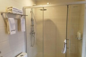 Cabina de ducha con paredes de vidrio, cabezal de ducha de mano y toallero con toallas dobladas.