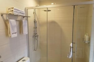 Cabina de ducha con paredes de vidrio, cabezal de ducha de mano y toallero con toallas dobladas.