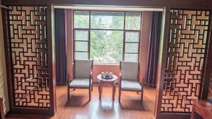 A room with a wooden floor, two chairs, a small table with a decorative item, and a window with a view of greenery. - Jiangcheng Lindeng Hotel (Jiangcheng)