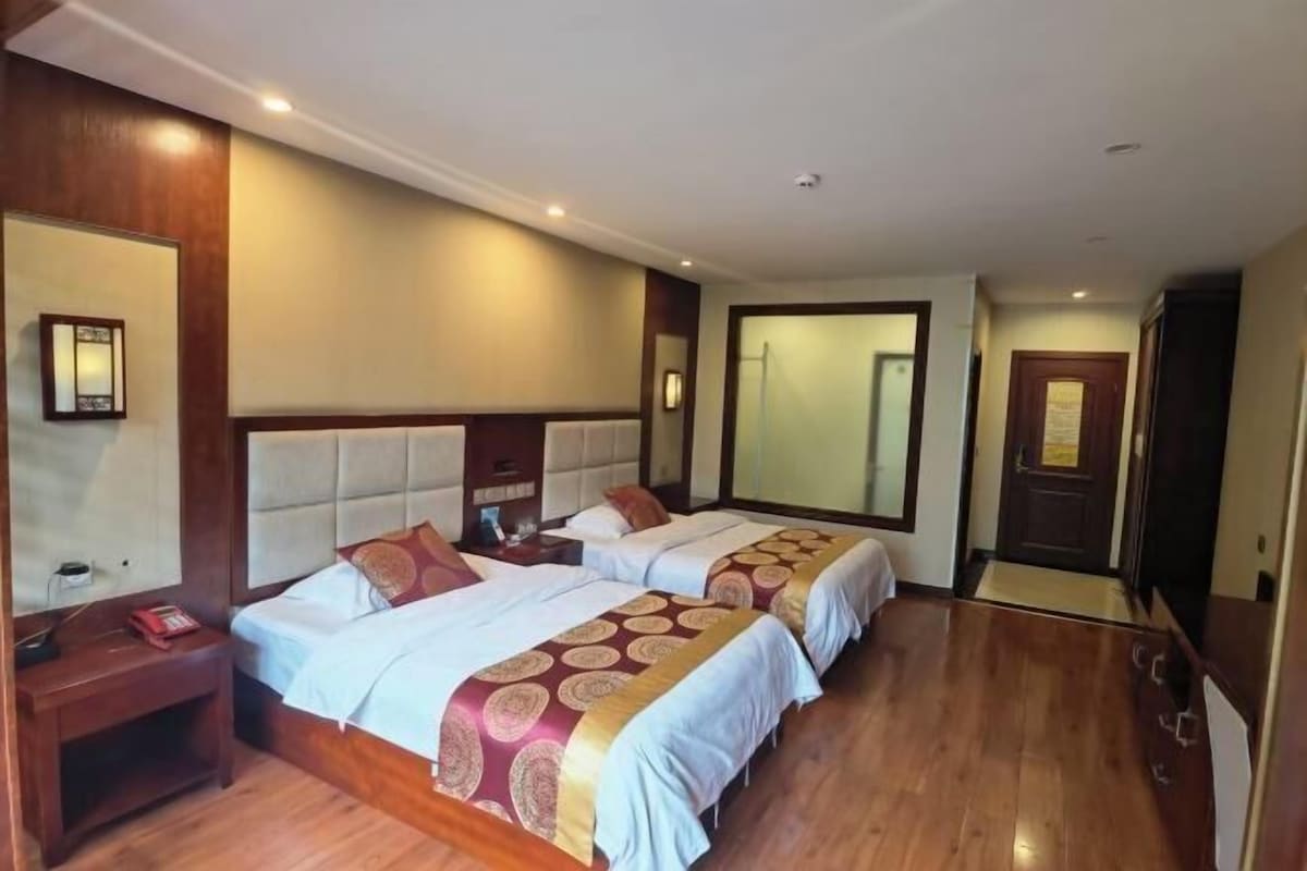 Una habitación de hotel con dos camas, suelo de madera, un espejo grande y una puerta.