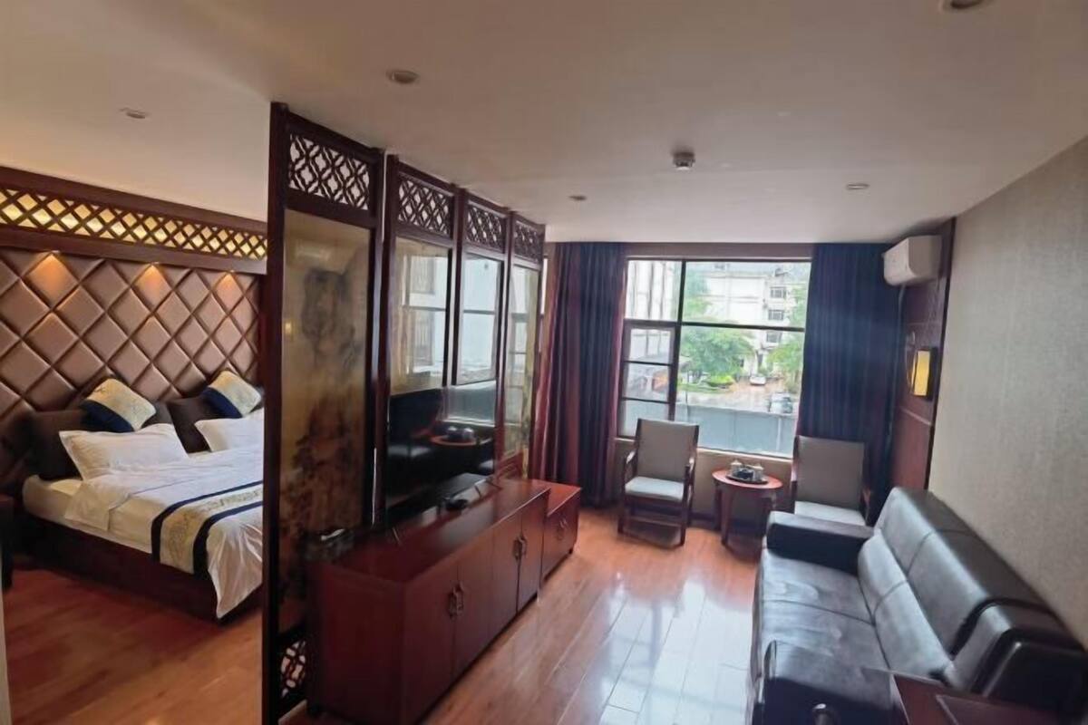 A hotel room with a bed, a TV, a sofa, a small table, and a view of the outside.