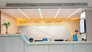 A reception desk with a modern design, a potted plant, and informational signs. - GT New Element Hotel (Ningbo)