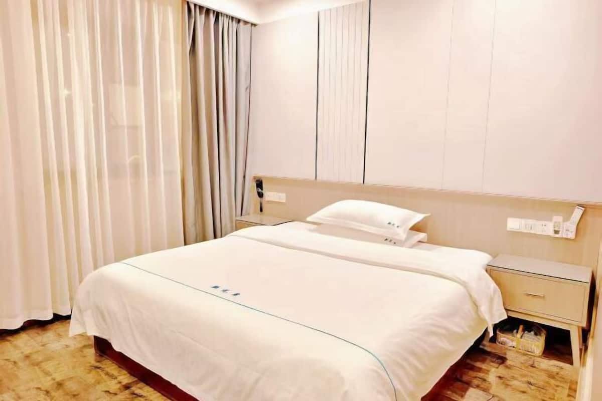 A hotel room with a bed, a nightstand, a lamp, and a curtain.
