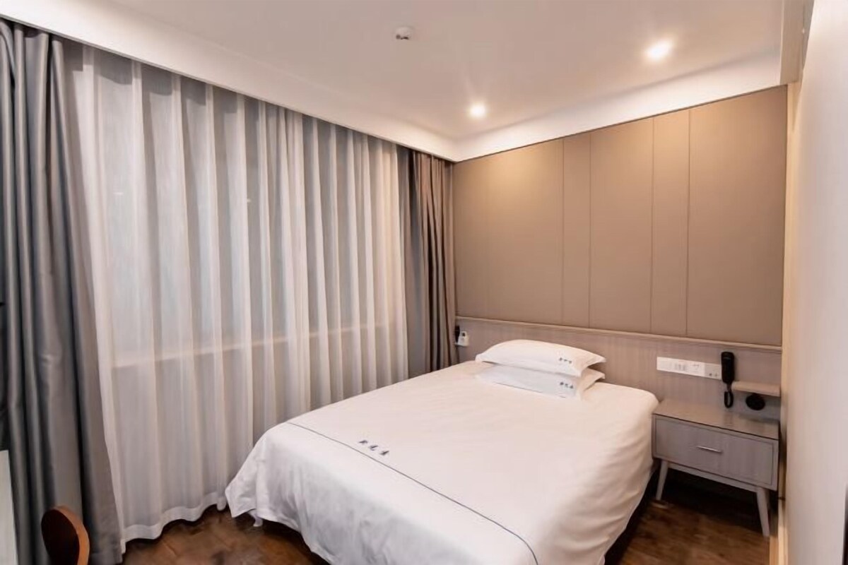 A hotel room with a bed, a bedside table, a telephone, and a curtain.