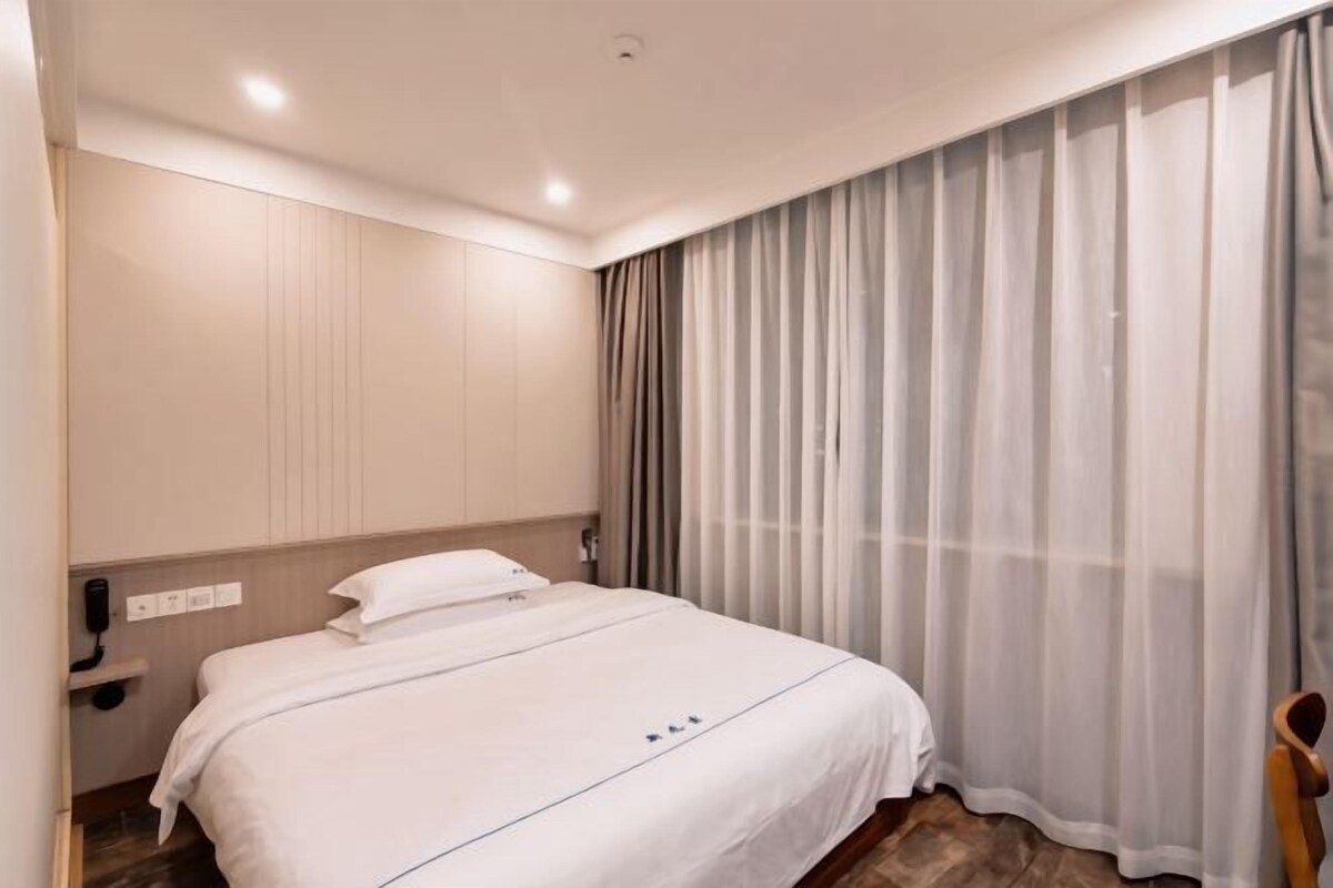 A hotel room with a bed, a nightstand, a chair, and a window with curtains.