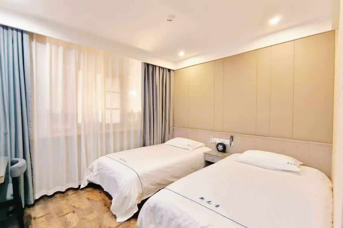 A hotel room with two beds, a desk, a chair, and a large window with curtains.