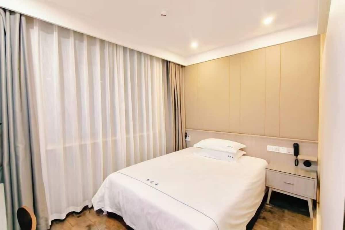 A hotel room with a bed, a bedside table with a phone, and a curtain.
