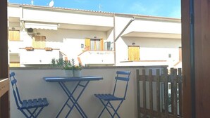 Ein Balkon mit Tisch und zwei Stühlen, ein Holzzaun und im Hintergrund ein Gebäude mit Balkonen.