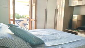 Ein Schlafzimmer mit Bett, Kissen, einem Fernseher und einer Schiebetür zu einem Außenbereich.